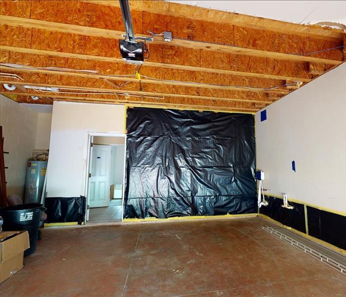 Garage with drywall ceiling removed and black plastic covering parts of the walls