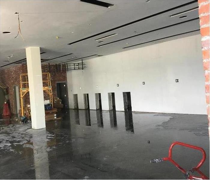 Large empty commercial room with concrete floors with puddles of water