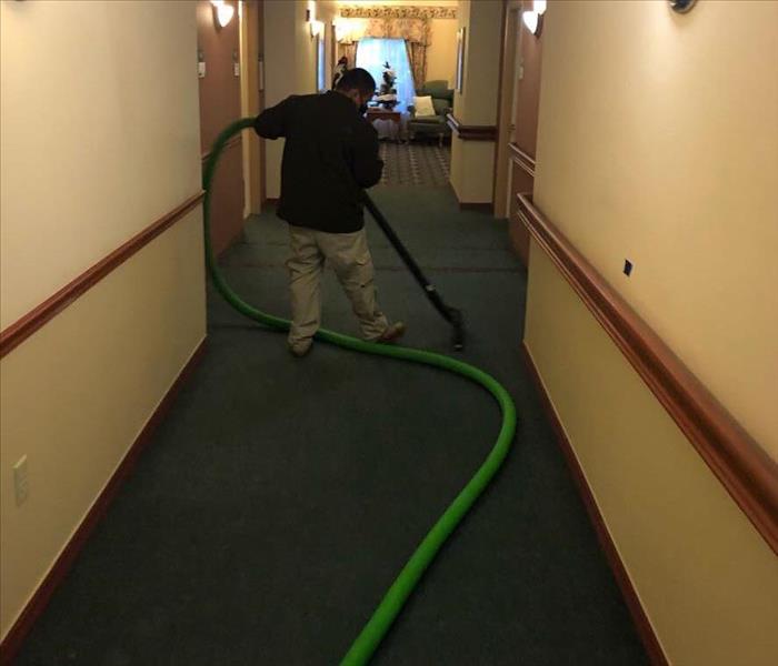 Technician using extraction wand to remove standing water in a flooded hallway