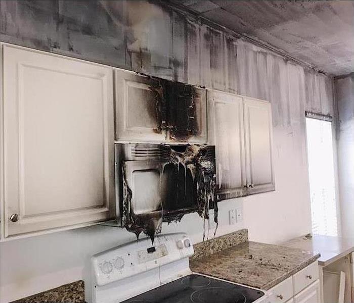 Burned microwave in a kitchen with white cabinets